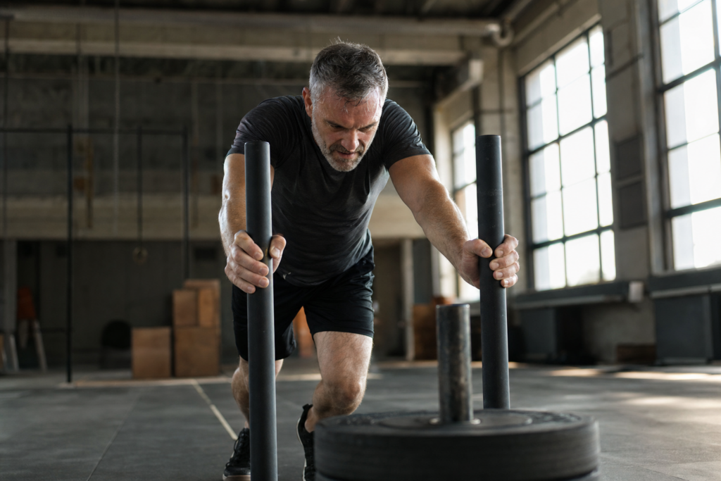 Mann Mitte fünfzig schiebt einen Gewichtsschlitten im Gym